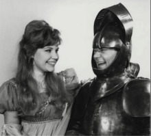 Publicity shot. Right: Reg Varney, in suit of arms with visor open. Left: Audrey Nicholson, smiling. The two are looking at each other happily.
