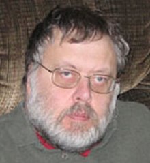 Middle-aged man wearing eyeglasses, a gray sweater, with black and gray hair, and a gray-haired beard