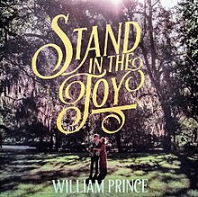 Picture of William Prince and his fiancée stood in a forest with the yellow text "Stand in the Joy" above them in ornate script.