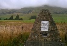 Memorial cairn near the graveyard which is in front of the trees to the left..