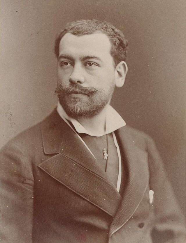 White man with dark hair and neat moustache and beard in smart 19th-century day clothes