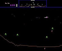 A horizontal rectangular video game screenshot that is a digital representation of a planet surface. A white, triangular spaceship in the upper right corner battles green alien enemies. The top of the screen features a banner that displays icons, numbers, and a miniature version of the landscape.