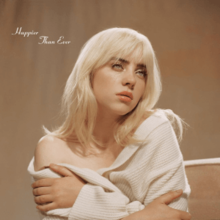 Cover art for Happier Than Ever: Billie Eilish with blonde hair and a white off-the-shoulder jacket, hugging herself. Behind her is a backdrop colored brown.