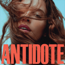 In red caps "ANTIDOTE" over a woman's calm face, partially covered by long brown hair blowing from her right side.