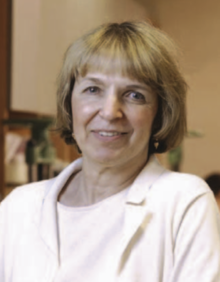 Photograph of Janice Merrill-Oldham - blond middle-aged woman in white shirt and blouse and smiling at the camera