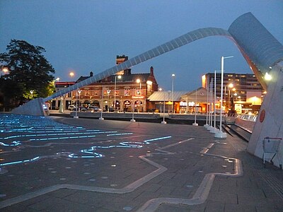 Millennium Square by night, showing the Time Zone Clock designed by Francoise Schein with the Whittle Arch soaring above