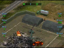 The player's "Apache" flies over the burning ruins of a building to attack an enemy structure, behind which enemy troops can be seen. The player's fuel, ammunition and armour levels can be seen at either side of the screen. Soviet Strike screenshot.png