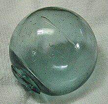 A Glass Fishing Ball Floats In Shallow Water, Bright Reflections