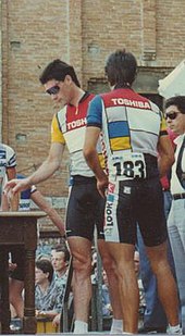 A man wearing a red, white, and blue cycling uniform while crossing his arms.