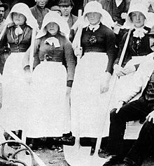 Four women in protective headdresses carrying large shovels