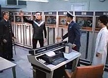 Using their "transponder" [sic], Dop, the Martian leader, wearing a poor-fitting skin diver's wet suit, materializes in the Space Center, attempting to explain his mission on Earth. Dop in Mars Needs Women.jpg
