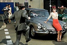 Cheryl reclining on the bonnet of a classic car while a gang of gents in 50s suits dance around her in the music video for "Under the Sun". Cheryl-cole-under-the-sun-video.jpg