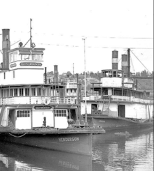 Logger, on right, distinctive for having two chimneys. Henderson, on left, with a single chimney, showing more common engineering layout, both at the dock of Shaver Transportation Company, in Portland, Oregon, in 1940. Sternwheelers Henderson and Logger in 1940.png