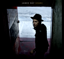 James Bay de pie en una puerta con un sombrero.