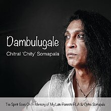 Image of Chitral Somapala against a black background. The words "Dambulugale" and "Chitral 'Chity' Somapala" are displayed next to his face. A translucent white banner covers the bottom inch of the image, with text displayed on top of it saying "The Spirit Goes On In Memory of My Late Parents PLA & Chitra Somapala".