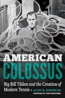 Book cover of "American Colossus: Big Bill Tilden and the Creation of Modern Tennis". Cover is over a photograph of Tilden wearing a suit, white collared shirt, and necktie with people standing out of frame holding tennis rackets arrayed around Tilden. In the lower half of the image is text that reads as follows: AMERICAN [line break] COLOSSUS [line break] Big Bill Tilden and the Creation of [line break] Modern Tennis • ALLEN M. HORNBLUM [line break] FOREWORD BY JOHN NEWCOMBE