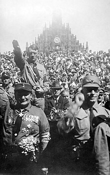 A monochrome image of a mass of people outside of a church facing the viewer performing Nazi salutes.