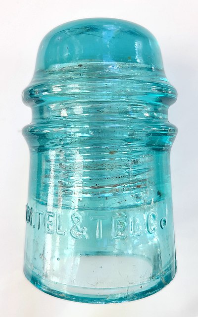 Pin-type glass insulator for long-distance open-wire transmission for telephone communication, manufactured for AT&T in the period from c. 1890 to WW-I; It is secured to its support structure with a screw-like metal or wood pin matching the threading in the hollow internal space. The transmission wire is tied into the groove around the insulator just below the dome.