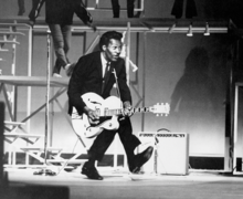 Rock 'N' Roll singer Chuck Berry doing a one-legged hop style "duckwalk" while playing the guitar. Chuck Berry Duckwalk.png