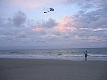 A man flying a kite on the beach, a good location for flying as winds travelling across the sea contain few up or down draughts which cause kites to fly erratically Man flying kite.jpg