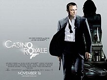 The poster shows Daniel Craig as James Bond, wearing a business suit with a loose tie and holding a gun. Behind him is a silhouette of a woman showing a building with a sign reading "Casino Royale" and a dark grey Aston Martin DBS below the building. At the bottom left of the image is the title "Casino Royale" – bothшп "O"s stand above each other, and below them is a 7 with a trigger and gun barrel, forming Bond's codename: "Agent 007" – and the credits.