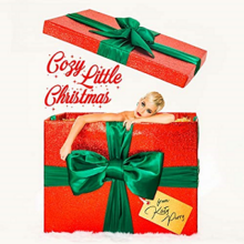 Katy Perry sobresaliendo de una caja de regalo roja con cintas decorativas verdes atadas a su alrededor.