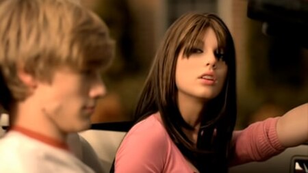 Swift portrays both the protagonist and the antagonist (seen here, a brunette cheerleader), and Lucas Till portrays the love interest in the music vid