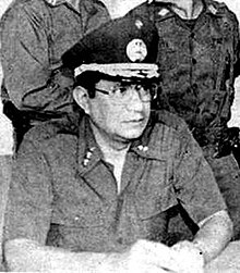 A black-and-white photograph of Jaime Abdul Gutiérrez wearing 1970s Salvadoran military uniform sitting at a table