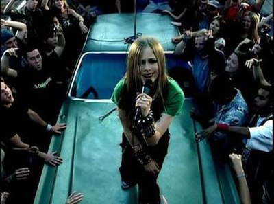 Lavigne, wearing her famous tie, sings on top of a car on the street.