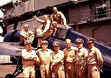 Nine members of the cast pose with a Grumman F4F Wildcat fighter on the flight deck of USS Lexington Midway FM2.jpg