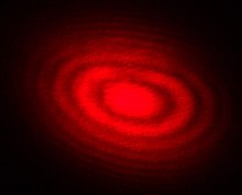 The local gravitational acceleration g is measured with exceptional precision with the help of a laser interferometer. The laser's pattern of interference fringes--the dark and light bands above--blooms at an ever-faster rate as a free-falling corner reflector drops inside an absolute gravimeter. The pattern's frequency sweep is timed by an atomic clock. Michelson Interferometer Laser Interference Fringes-Red.jpg