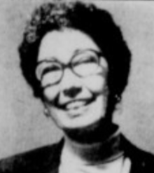 A smiling white woman with short curly hair and glasses