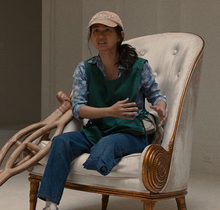 A Vietnamese woman wearing a cap with her left leg missing below the knee sits in a chair with wooden crutches next to her.