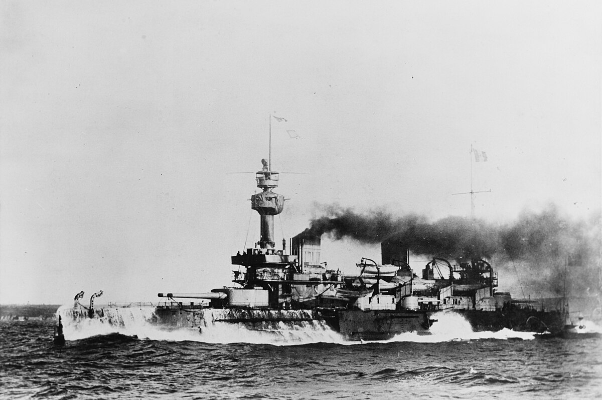 French battleship Brennus, seen with water cascading off its sides. All the usual features of French battleships of the time - ie terrible ones - are present. This includes tumblehome and enough naval junk to equip two regular fleets.