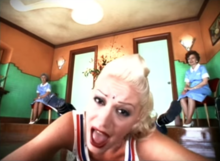 Stefani wearing a bindi and dancing around the clean ladies' restroom surrounded by female attendants in the "Just a Girl" video. No Doubt "Just a Girl" music video.png