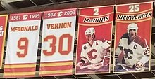 Quattro striscioni rettangolari sono appesi alle travi in ​​un'arena di hockey.  I due all'estrema sinistra sono prevalentemente bianchi con finiture rosse e dorate.  Quella di sinistra dice "1981–1989 McDONALD 9" e quella di destra "1982–2002 VERNON 30".  Sul lato destro di essi sono mostrati altri due banner.  Entrambi sono principalmente rossi, ognuno mostra (dall'alto verso il basso) un numero, poi uno striscione rosso con finiture dorate che mostra un nome, e infine una persona in completo abbigliamento da hockey, che viene mostrata con indosso una maglia bianca con finiture rosse e un casco bianco .  Quello di sinistra dice "2 MacINNIS", mentre quello di destra dice "25 NIEUWENDYK".