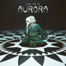 Aurora is wearing green clothing and sitting on a black-and-white tiled floor. She is holding a mask that partially covers her face while looking forward. Above her, the words "Cure for Me" and "Aurora" are placed in all caps.