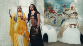 Gaga in a yellow dress, with two characters who are guiding her through the video. The painting in the background foreshadows the twist ending of the clip, and is reminiscent of some of Frida Kahlo's work. Lady Gaga - 911 (music video screenshot).png