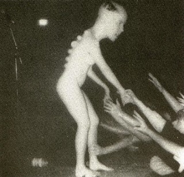 Kathleen Lynch, naked dancer, greeting Butthole Surfers fans on the front cover, slightly deformed with a bigger head and an alien-like spine compared