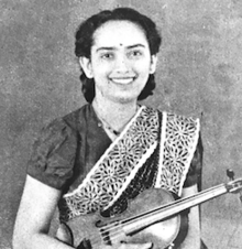 A smiling young South Asian woman, holding a violin and wearing a sari
