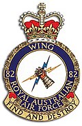 Military crest of No. 82 Wing RAAF, topped with a crown and featuring a mailed fist holding two lightning bolts, beneath which appears the phrase 