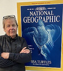 Curtsinger in front of a large print of his February 1994 cover on National Geographic, showcasing a long exposure of a sea turtle underwater. c. 2023 Bill curtsinger sea turtle cover national geographic 2023.jpg