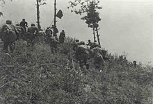 Joukko sotilaita ryntämässä mäkeä lipunkannattaja johdossa