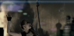 Still from the music video "Pop Diva", showing Koda hanging from a rope and being hauled away by an airship. Pop Diva Music Vide.png