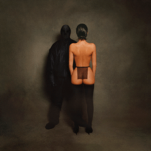 A photograph of West completely obscured by all-black clothing (including an opaque head covering) standing next to his wife Bianca with her back turned, wearing stockings and a sheer black cloth around her waist