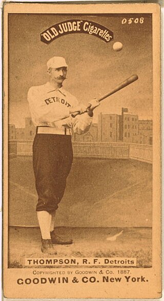 A sepia-toned image of a mustachioed man wearing an old-style baseball uniform holding a baseball bat