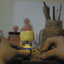 A pair of hands holding ornaments of a lamp and a moth.