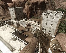 A scene viewed from first person; a man representing the player holds a rifle while looking down from a high vantage point on a castle structure with vehicles parked in its courtyard. An ammunition counter and reload command is visible in the bottom right corner.