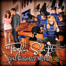 Photographie d'un terrain de basket d'un lycée, avec un couple à gauche et une fanfare à droite.  Le nom "Taylor Swift" est imprimé en cursif et le titre "You Belong with Me" est imprimé au bas de l'image.