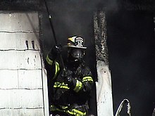 Volunteer fire fighter exiting live burn structure wearing NIOSH-certified SCBA, NFPA compliant turn-out gear, and holding a pike pole Volunteer Fire Fighter.jpg